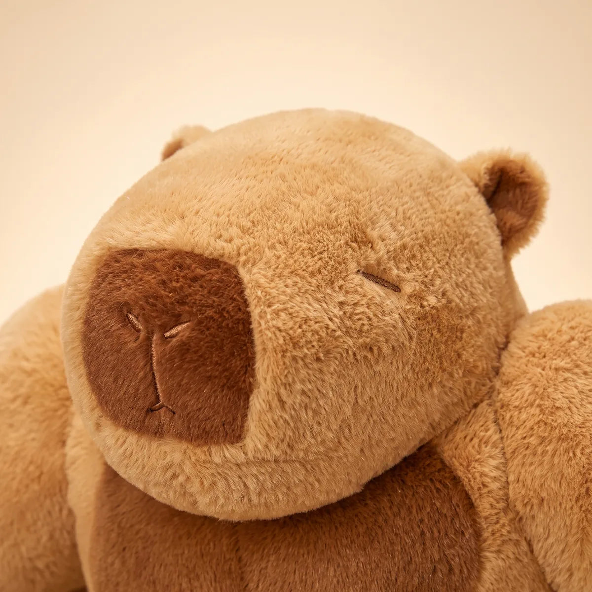 Close up of the embroidered sleeping face and brown muzzle of the buff capybara plush