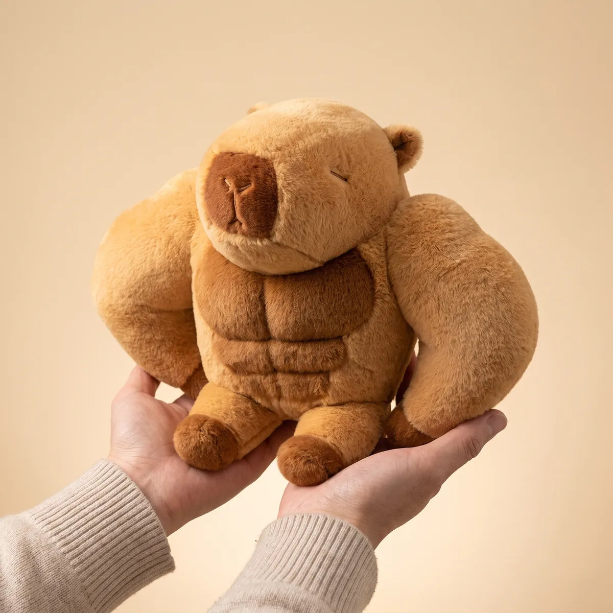 Two hands holding the buff capybara plush from below to show how wide its arms sit