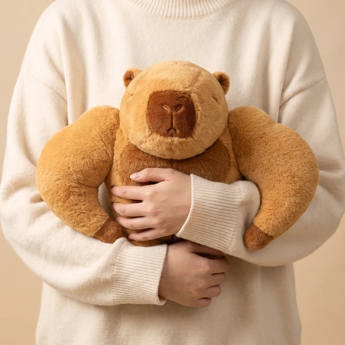Person hugging the buff capybara plush against a cream sweater, its arms sticking out on both sides