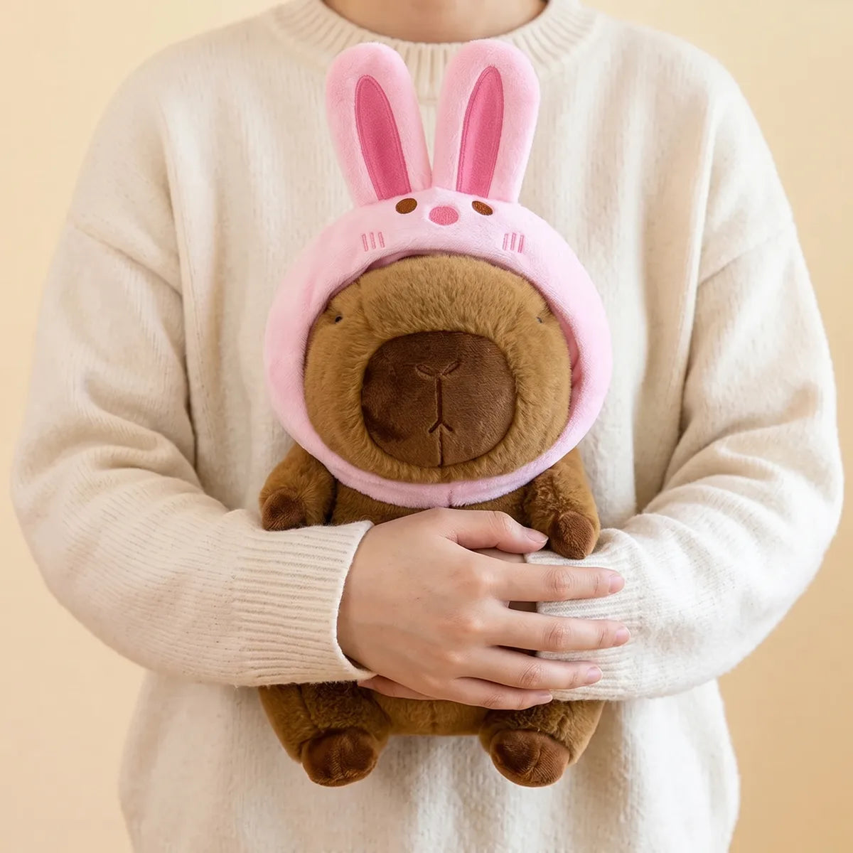 Person hugging the bunny capybara plush against a cream sweater