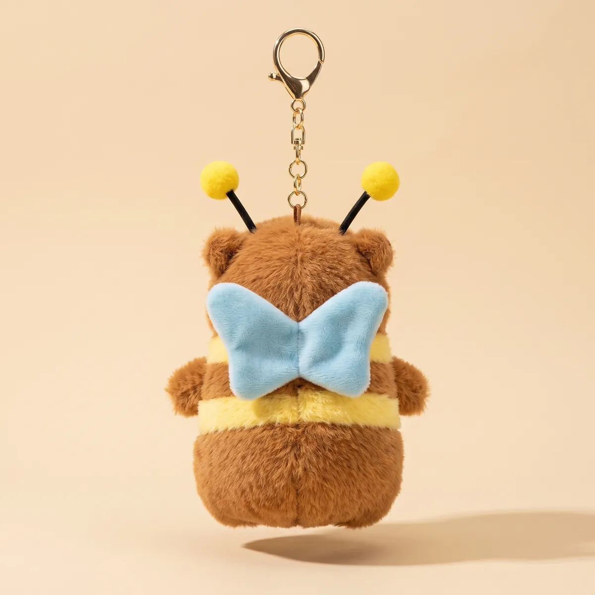Back of the capybara bee keychain plush showing the pale blue plush wings and the yellow band across the body