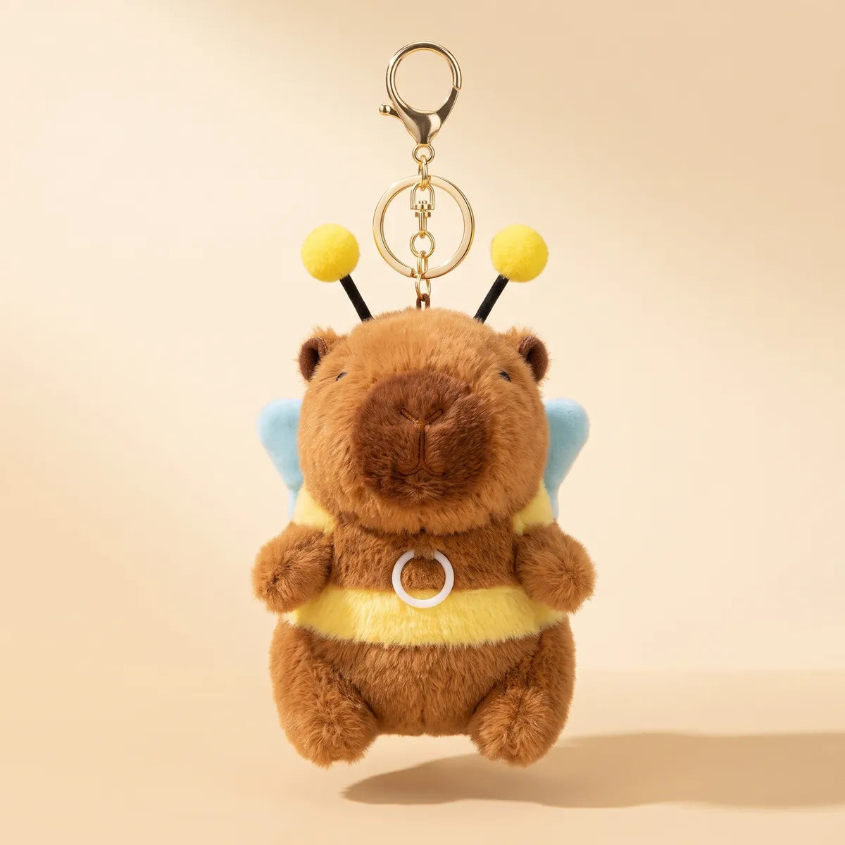 Front view of the 5 in capybara bee keychain plush hanging from its gold ring, the clear plastic ring on its yellow belly band, on a plain beige background