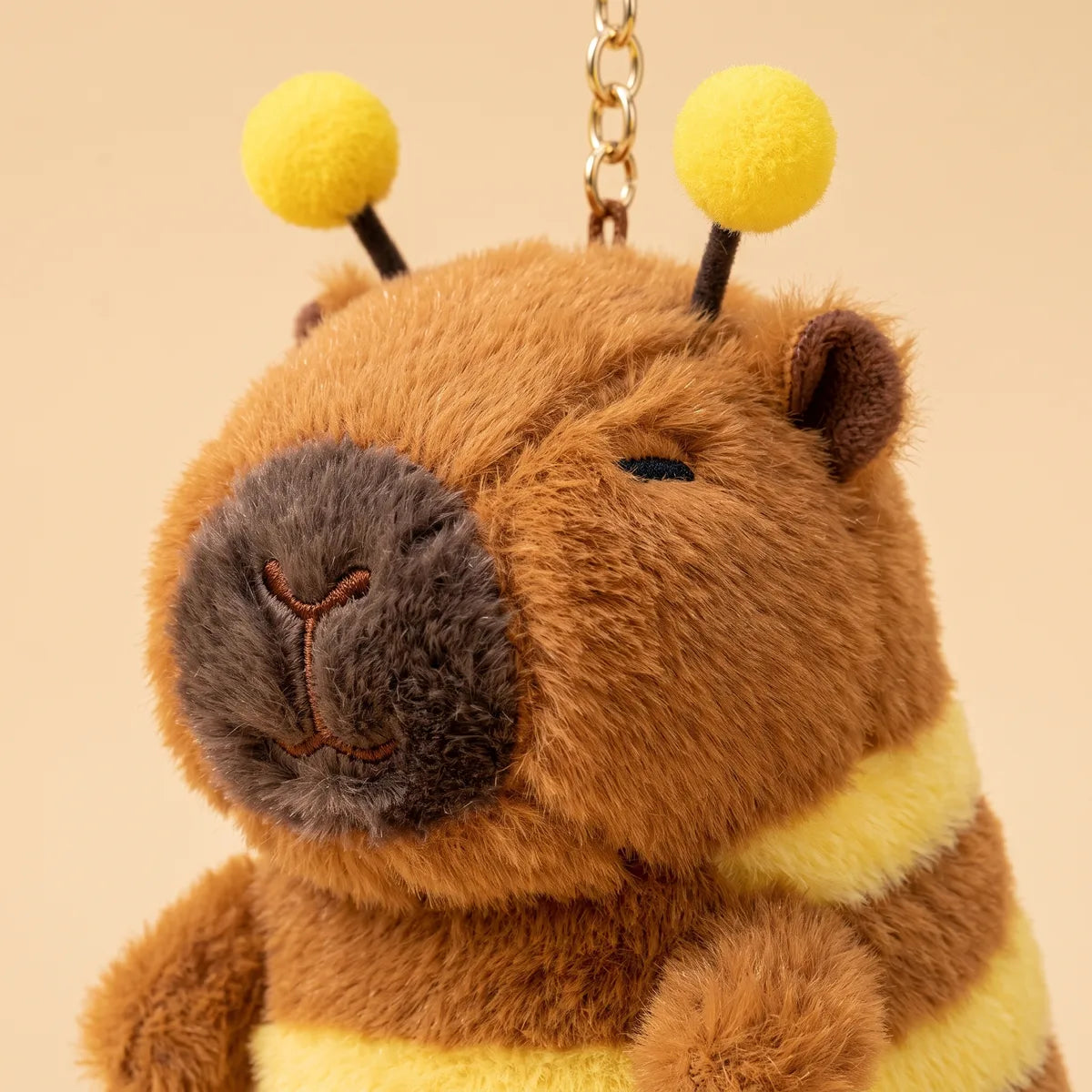 Close up of the capybara bee keychain plush head with yellow pom pom antennae and embroidered eyes