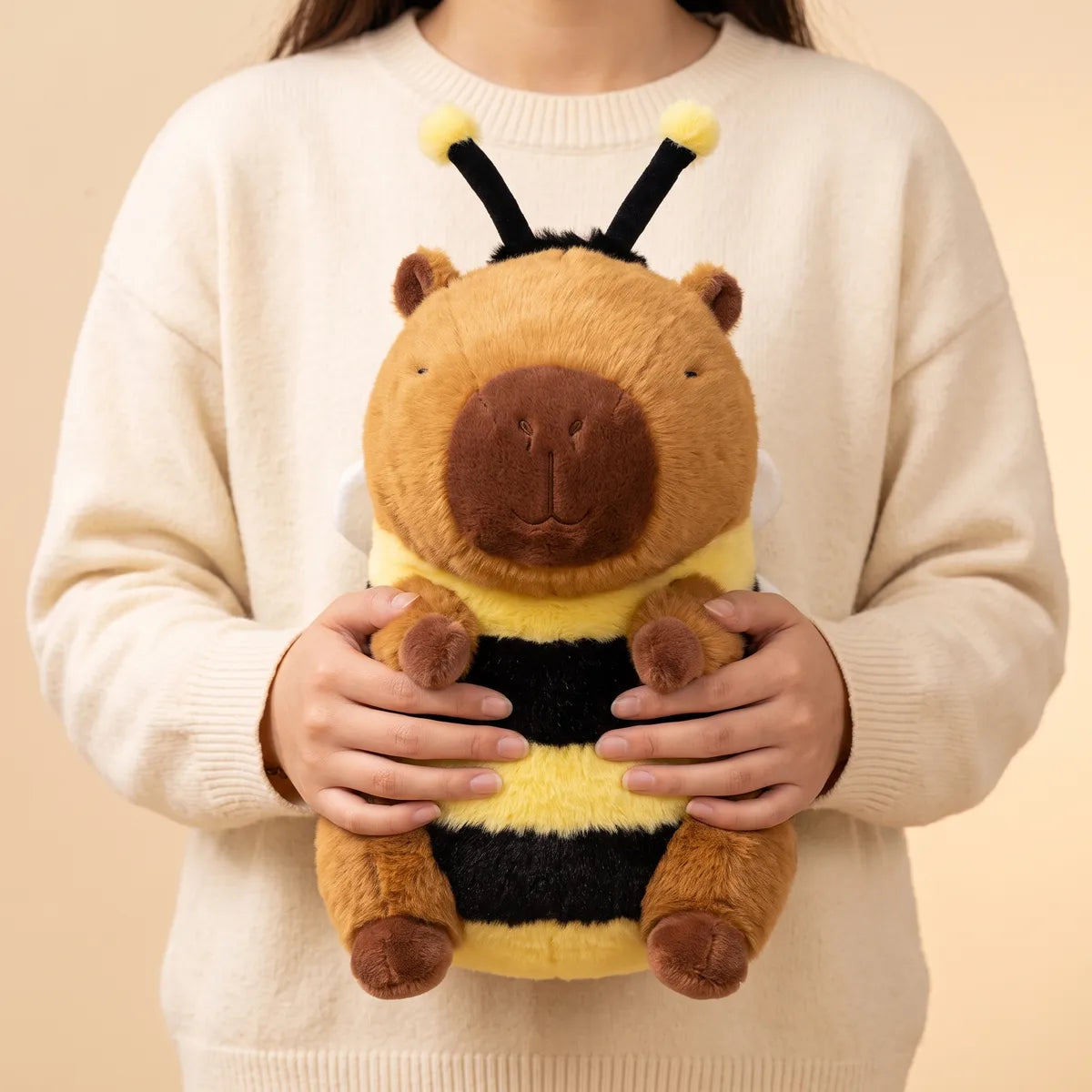 Capybara bee plush carried in both hands with the yellow and black stripes facing out and one white wing visible