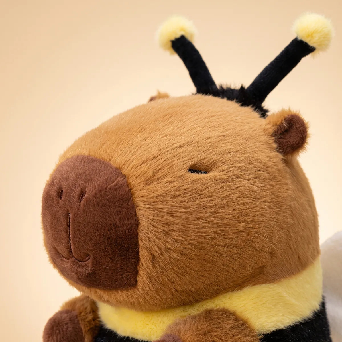 Close up of the capybara bee plush head showing the dark brown muzzle, embroidered eyes and black antennae