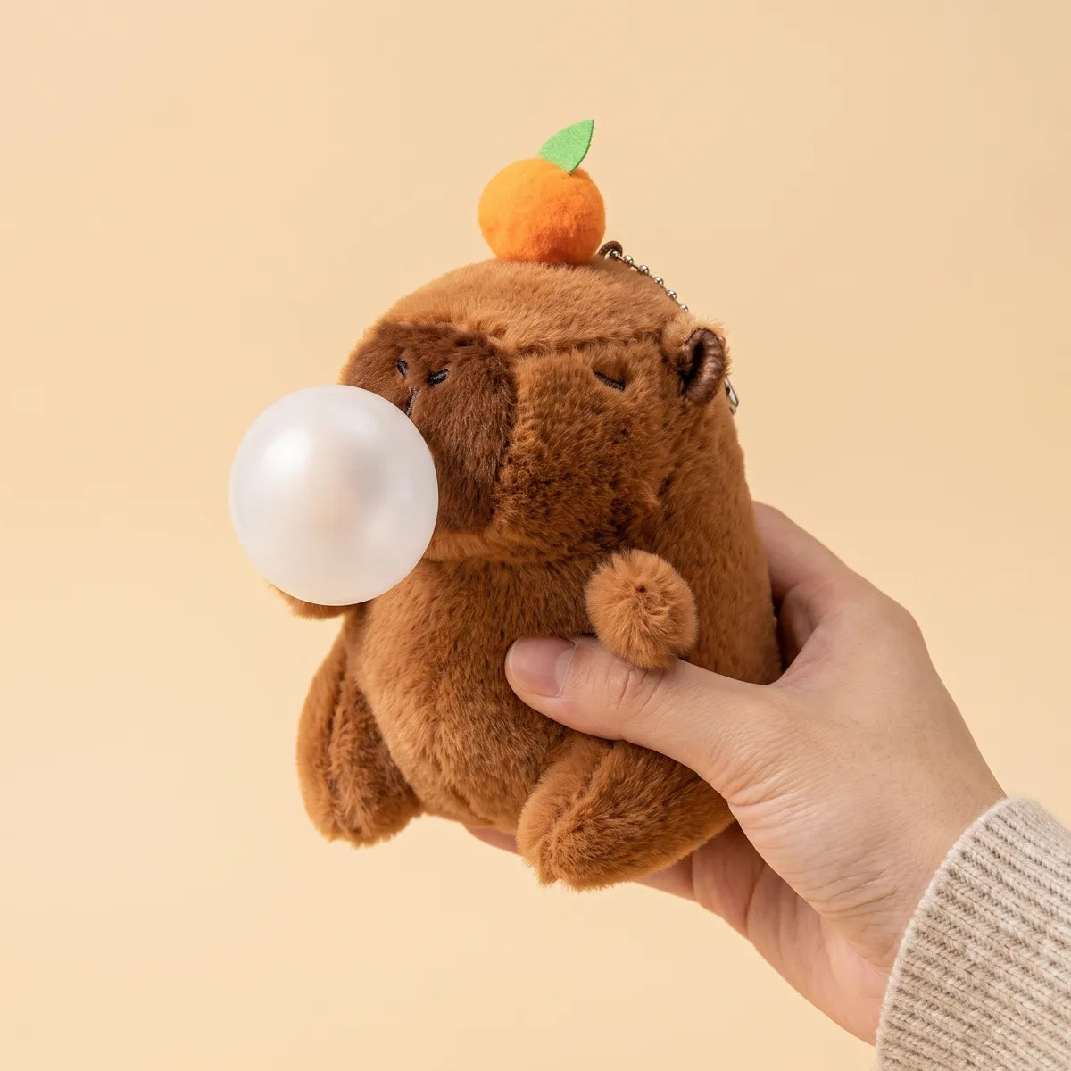 Capybara blowing bubble keychain plush held in one hand, the pearly white bubble at its muzzle blown large