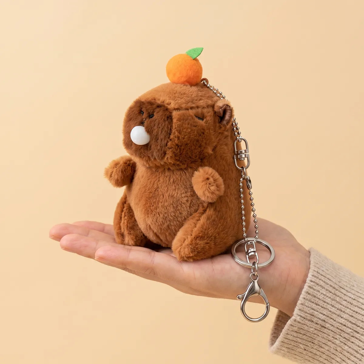 Capybara blowing bubble keychain plush sitting flat on an open palm with its ball chain and lobster clasp hanging down.