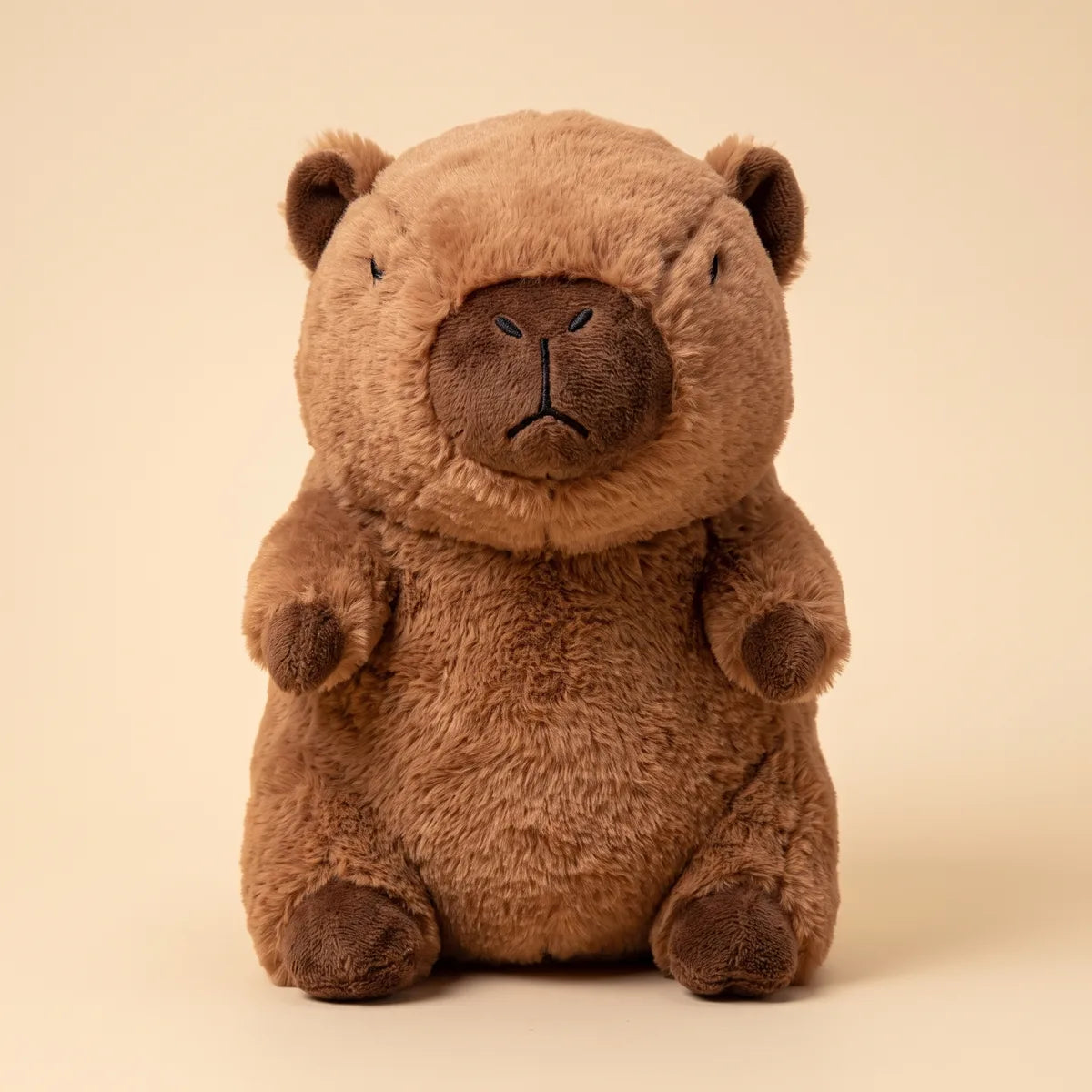 Brown capybara breathing plush photographed head on, seated upright with a dark muzzle patch and four dark paws.