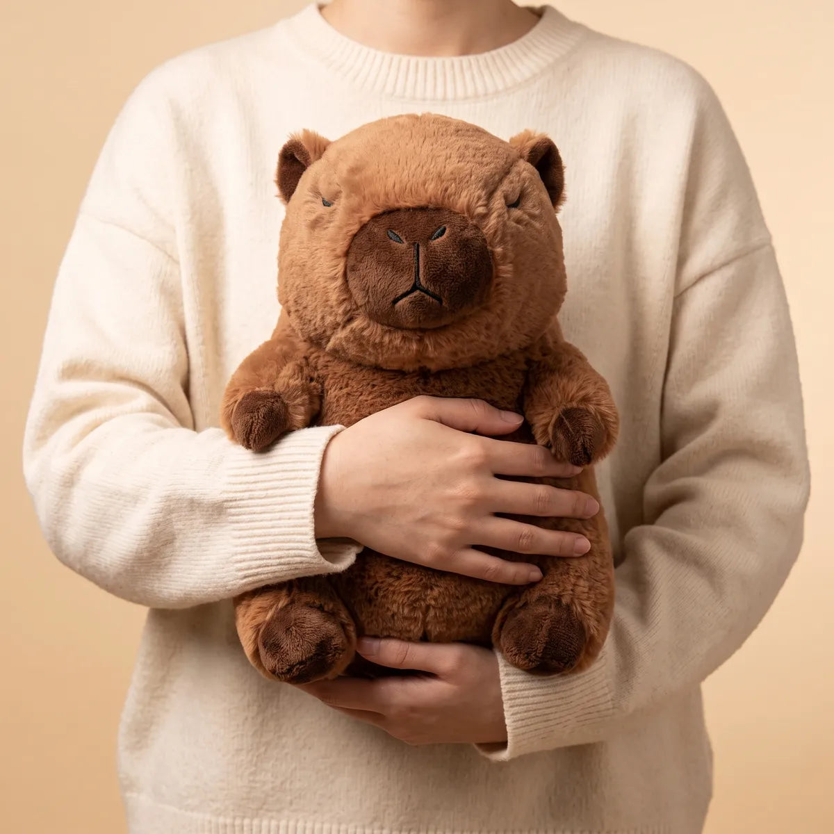 Capybara breathing plush held against a chest between two forearms, its whole front from the head to the four dark paws still in view