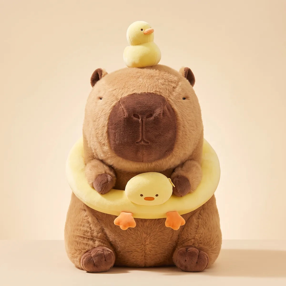Front studio view of the capybara duck plush wearing its pale yellow duck swim ring, the duckling head on the ring closed by a gold zip