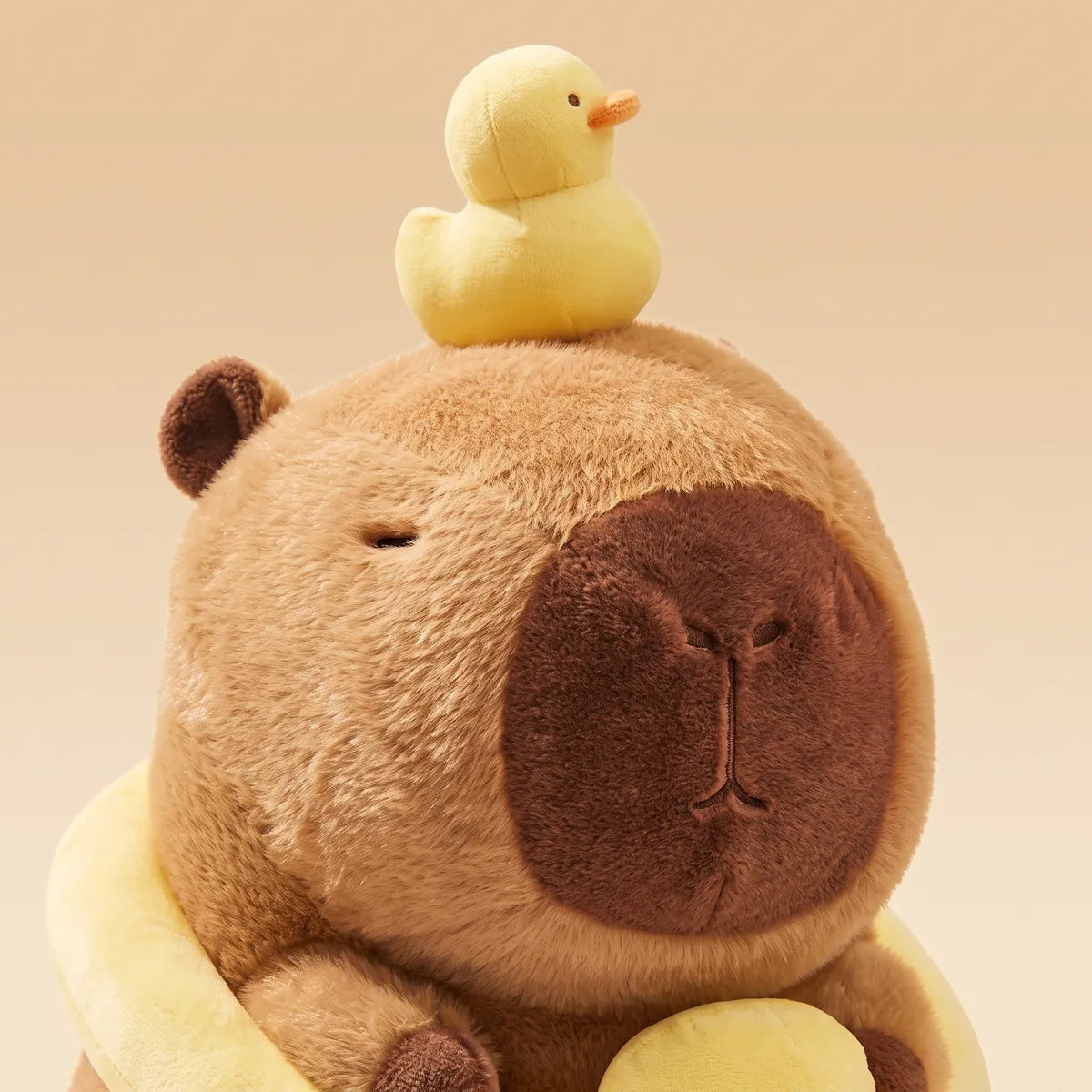 Close-up of the capybara duck plush head with the pale yellow duckling perched on the crown and the chocolate brown muzzle below