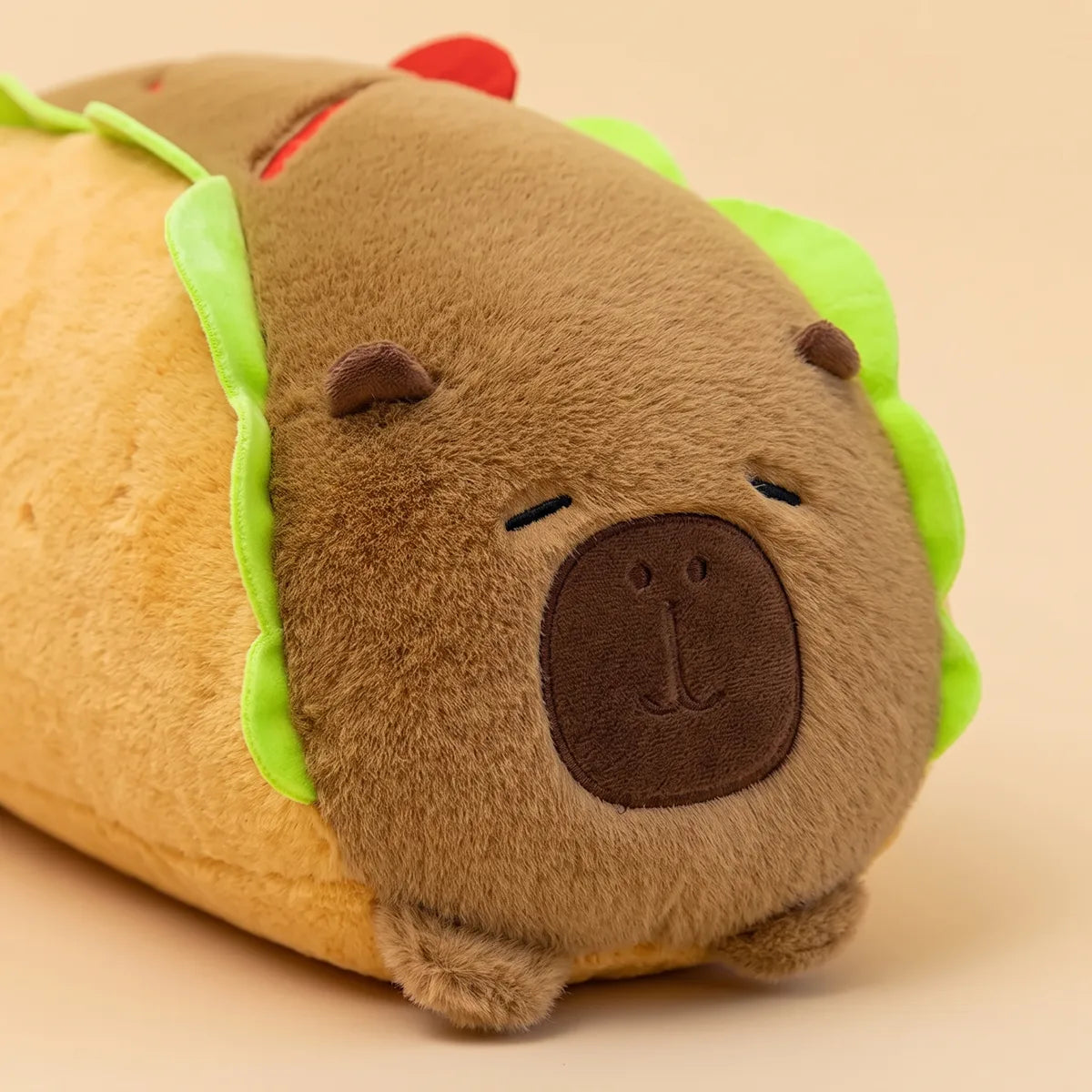 Close up of the sleeping face on the capybara hot dog plush, dark brown muzzle patch and closed eyes stitched in black thread