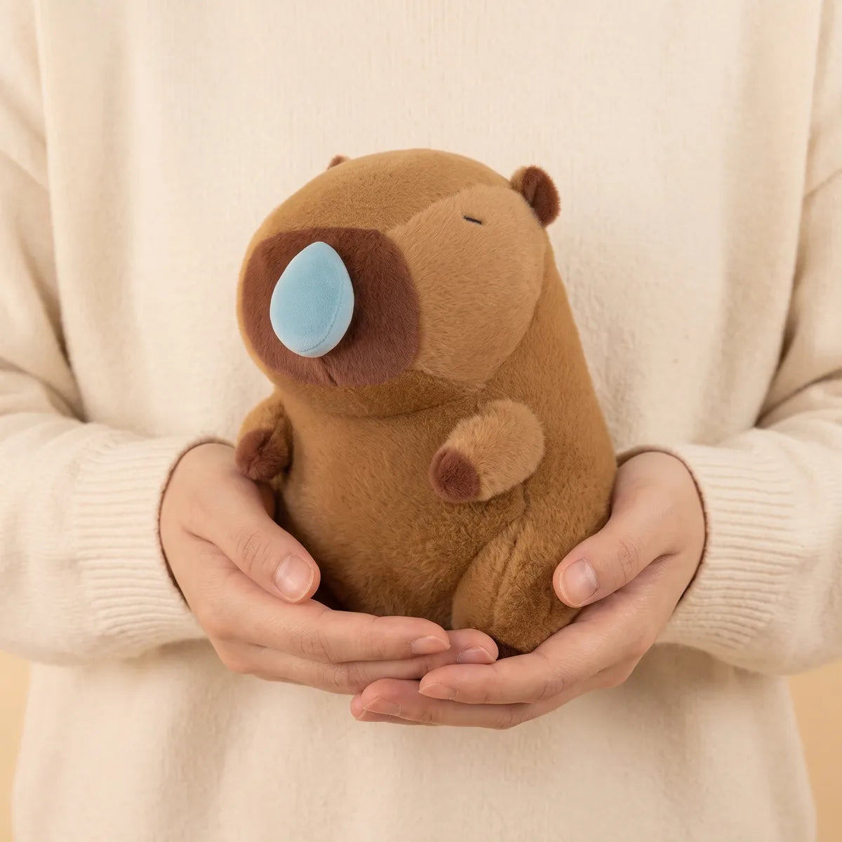 Person holding the capybara snot plush against a cream knit sweater, its blue bubble facing out