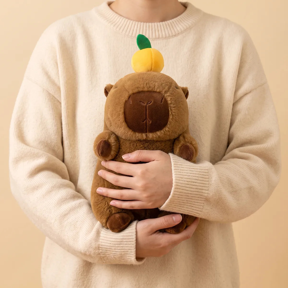 Person holding the capybara with orange on head plush against a knit sweater