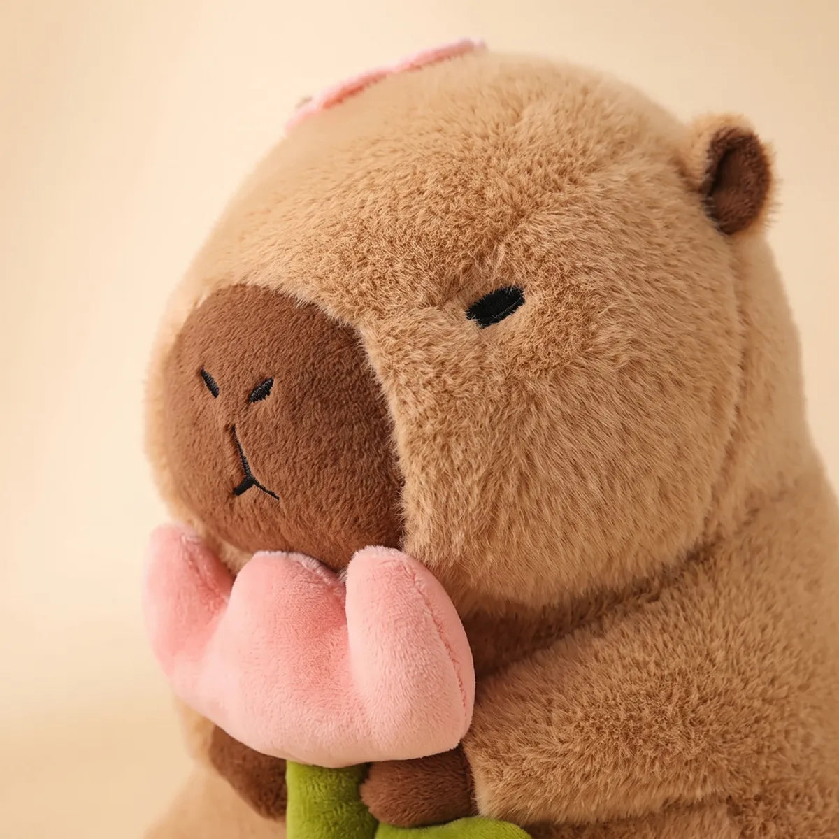 Close up of the capybara with rose plush face and the single pink petal resting on its head