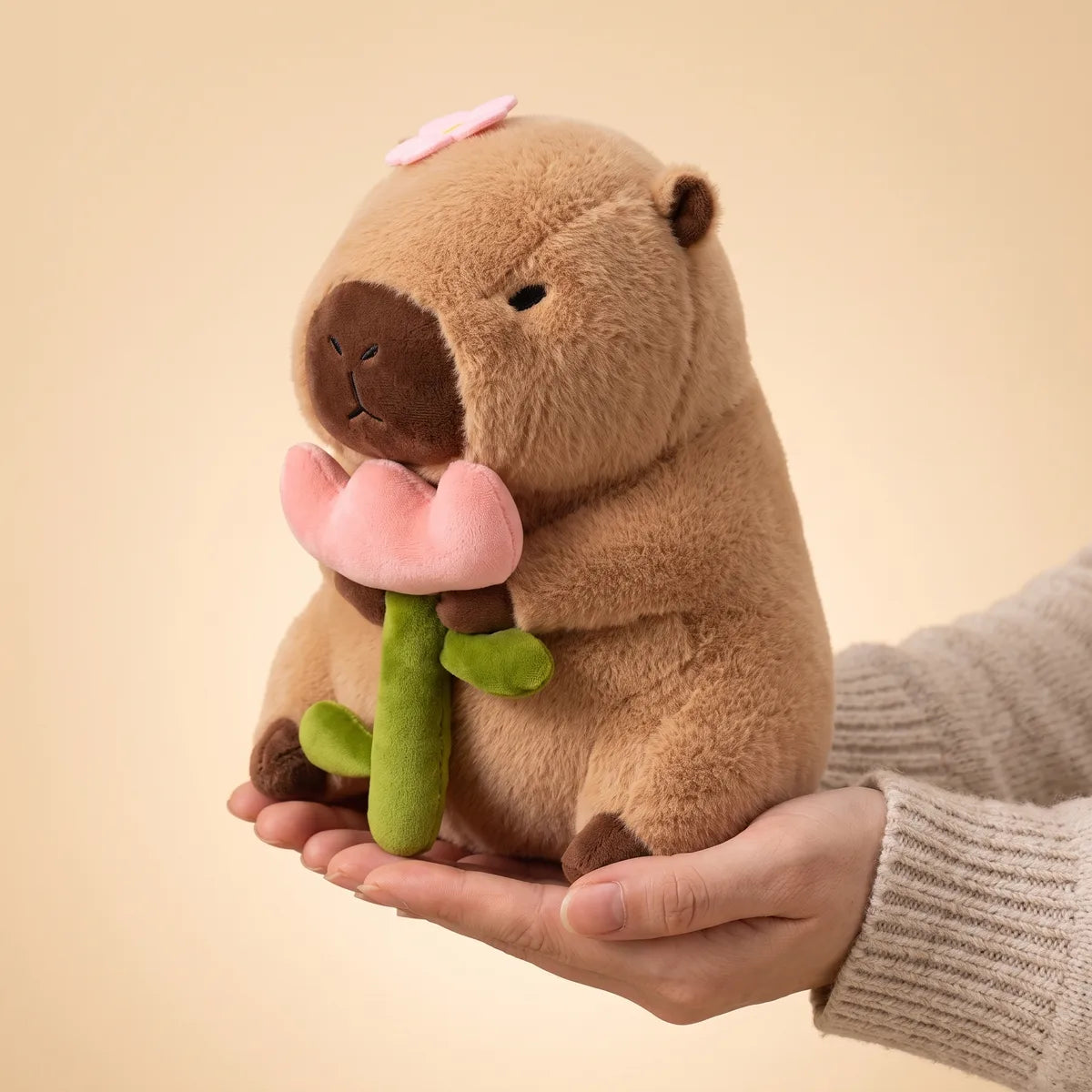 Hands cradling the 12 in capybara with rose plush to show its real size