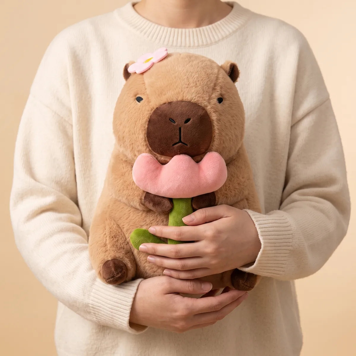 Person hugging the capybara with rose plush against a knit sweater, the bloom facing out