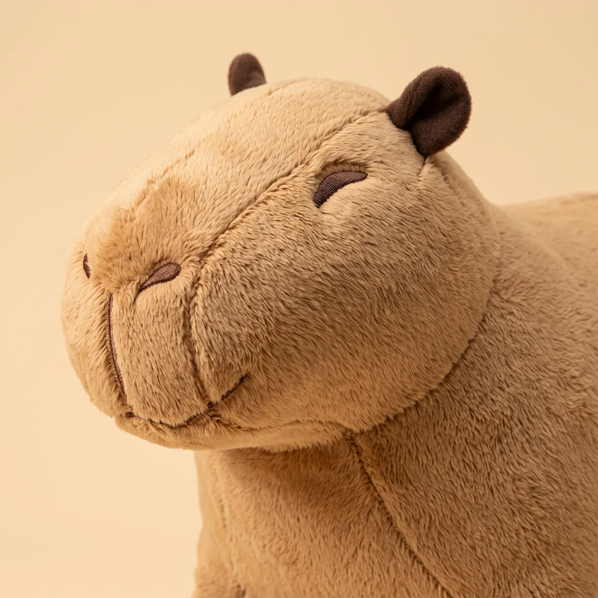 Close-up of the tan mother capybara plush head with dark brown ears and closed stitched eyes