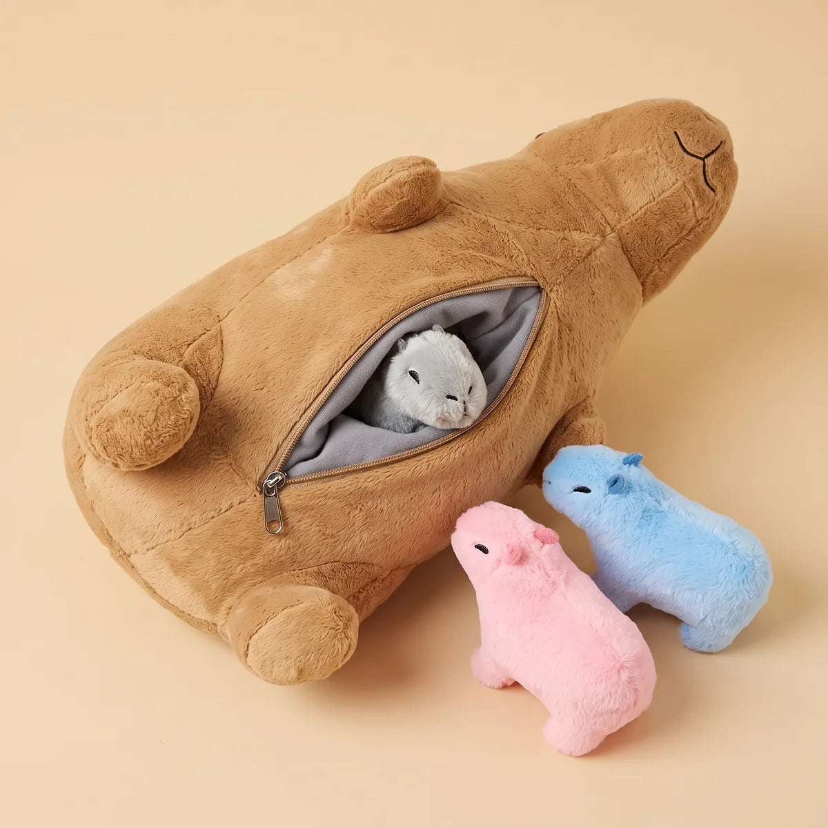 Zippered belly pouch of the mother capybara plush opened, with a grey baby tucked inside and pink and blue babies beside it