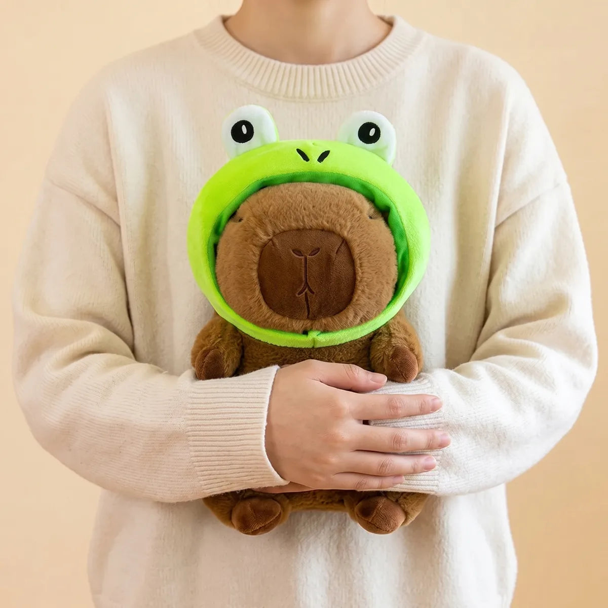 Person hugging the frog capybara plush against a sweater