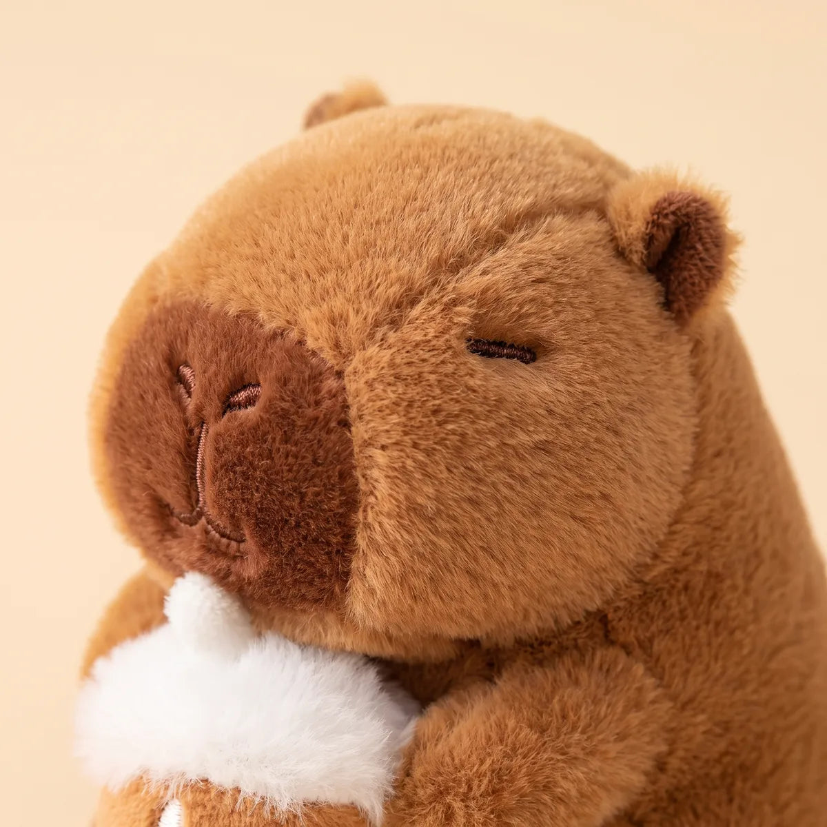 Close-up of the hazelnut mini capybara plush face with a dark brown muzzle and stitched closed eyes