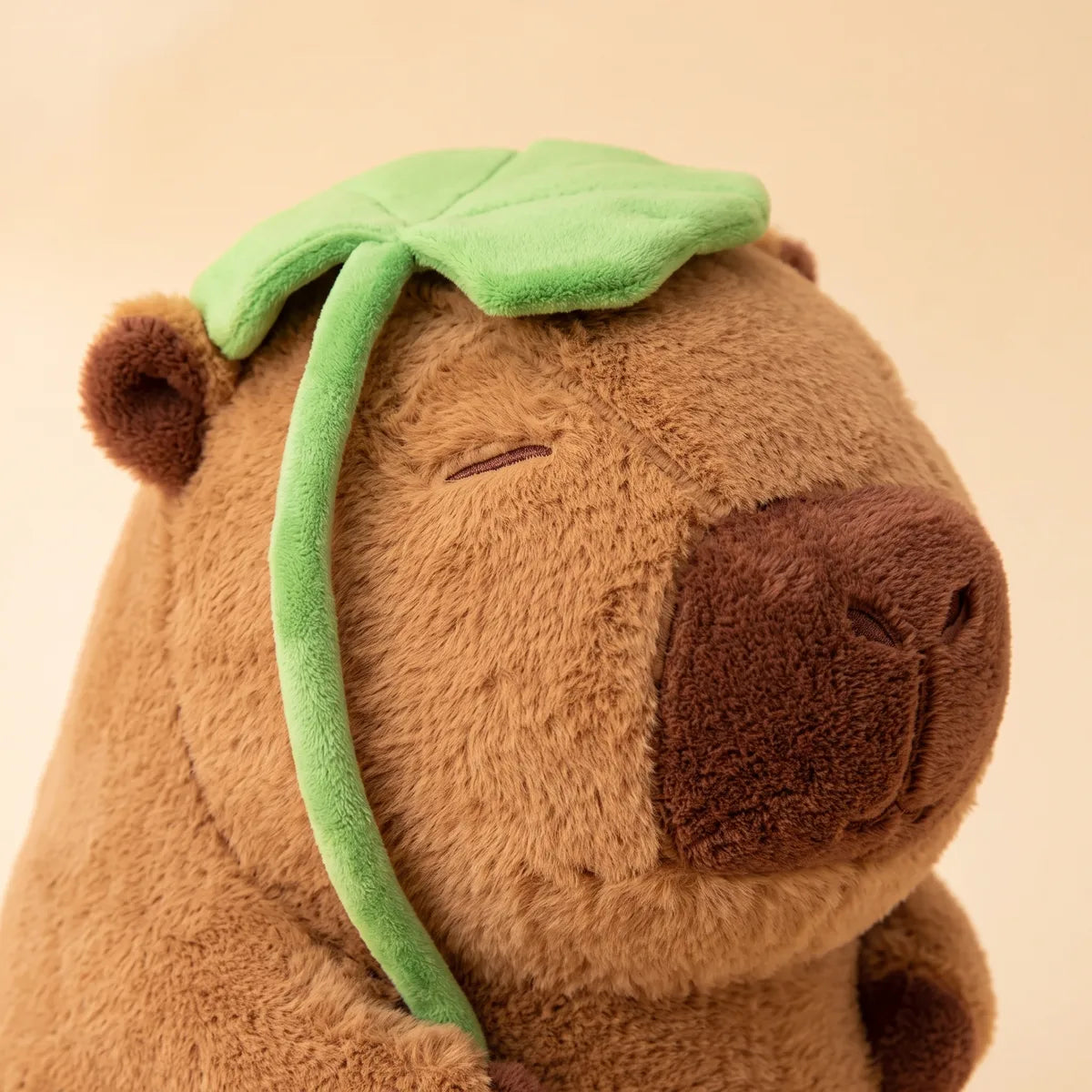 Close up of the jumbo capybara plush head showing the green plush leaf, its stalk and the dark brown muzzle.