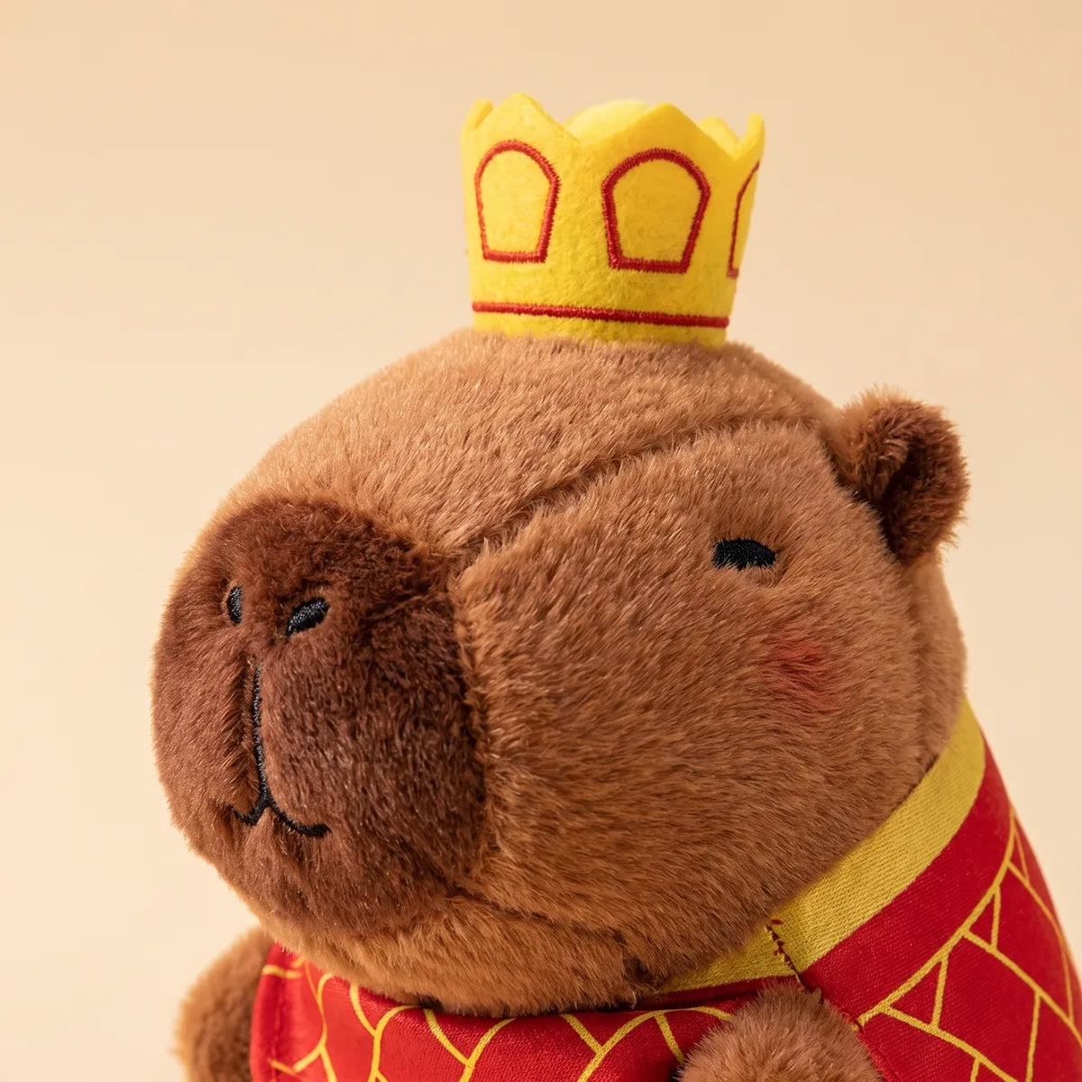 Close-up of the mini capybara plush yellow crown, stitched closed eyes and pink blushed cheeks