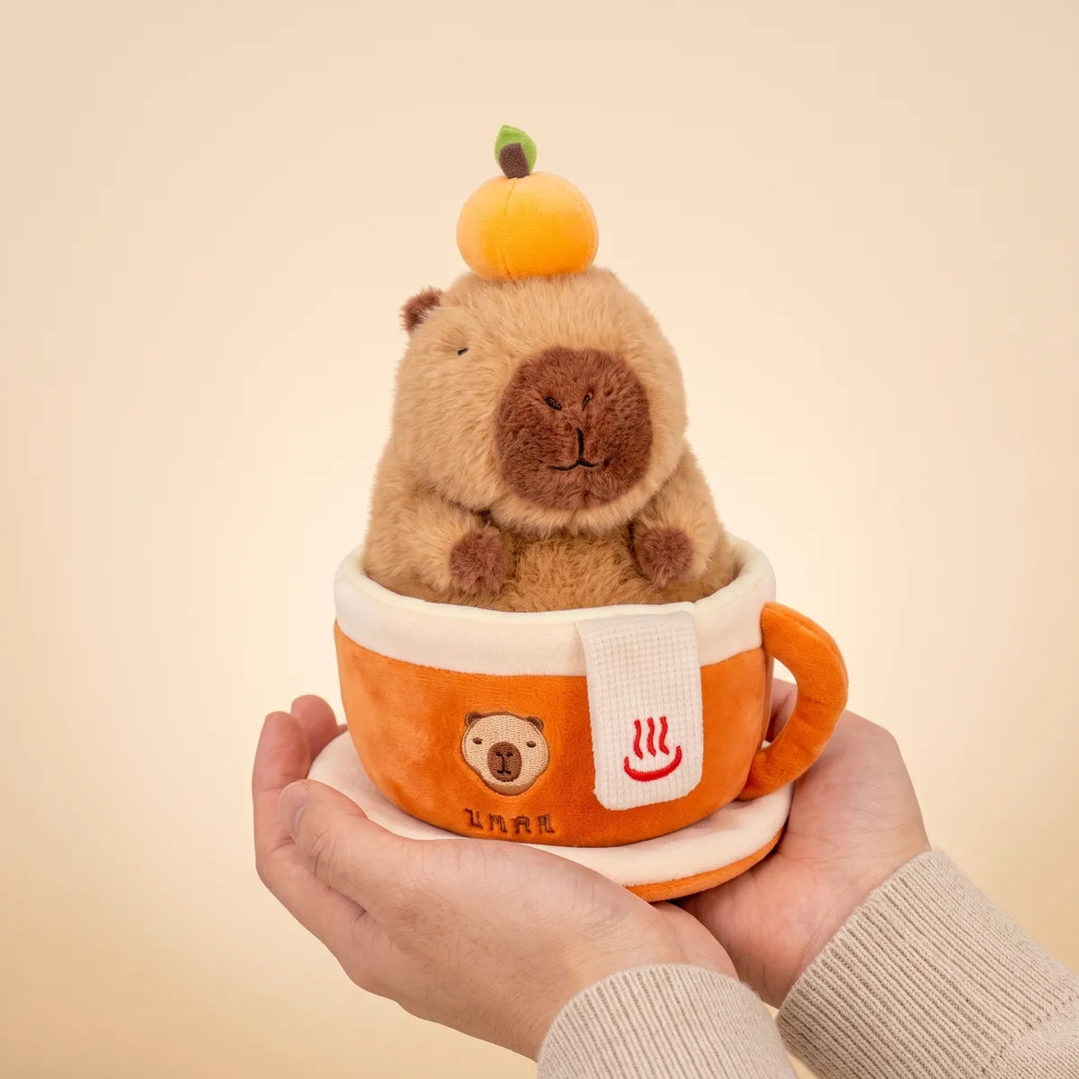 Hands cradling the orange coffee cup capybara plush to show its real size