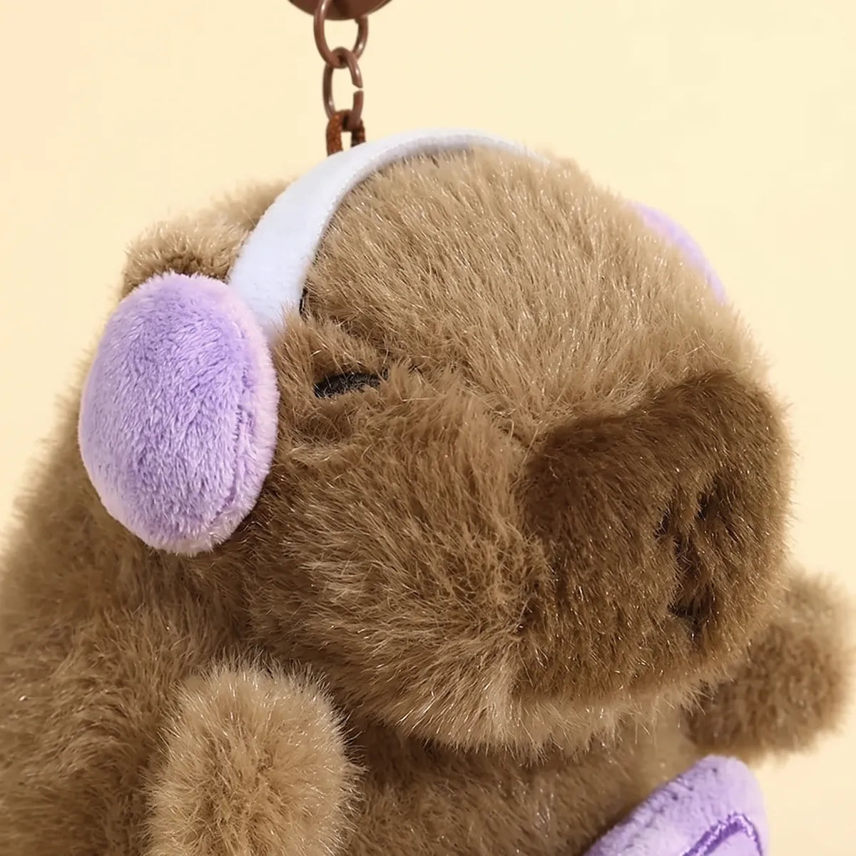 Close-up of the piano capybara keychain wearing lilac padded headphones on a white band