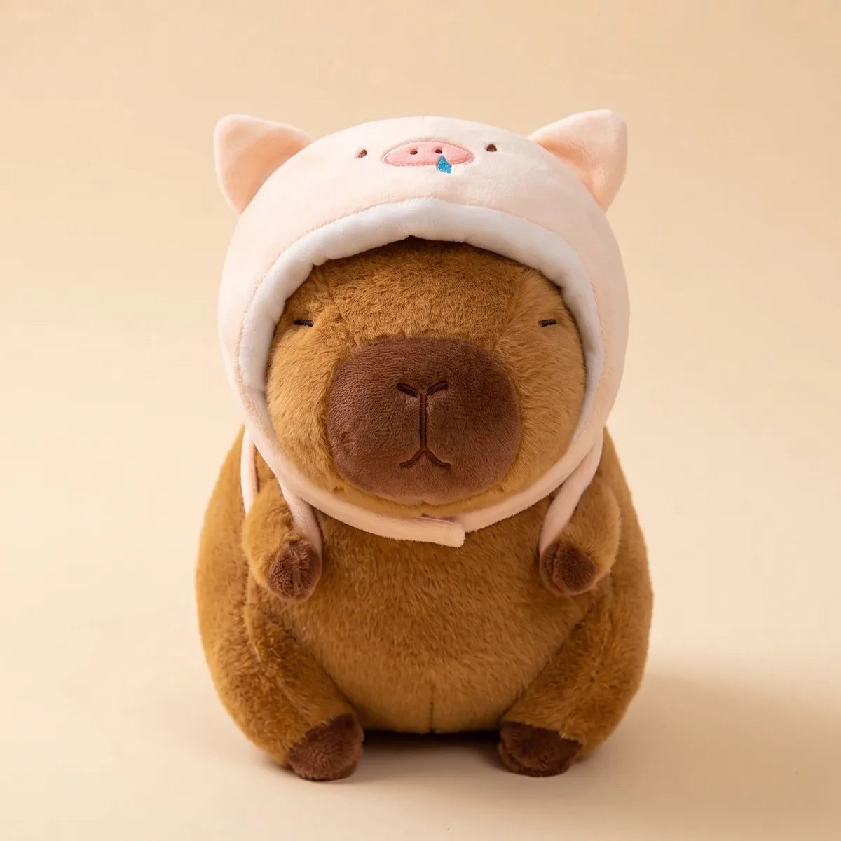 Brown piggy capybara plush seen from the front in its pale pink pig hood