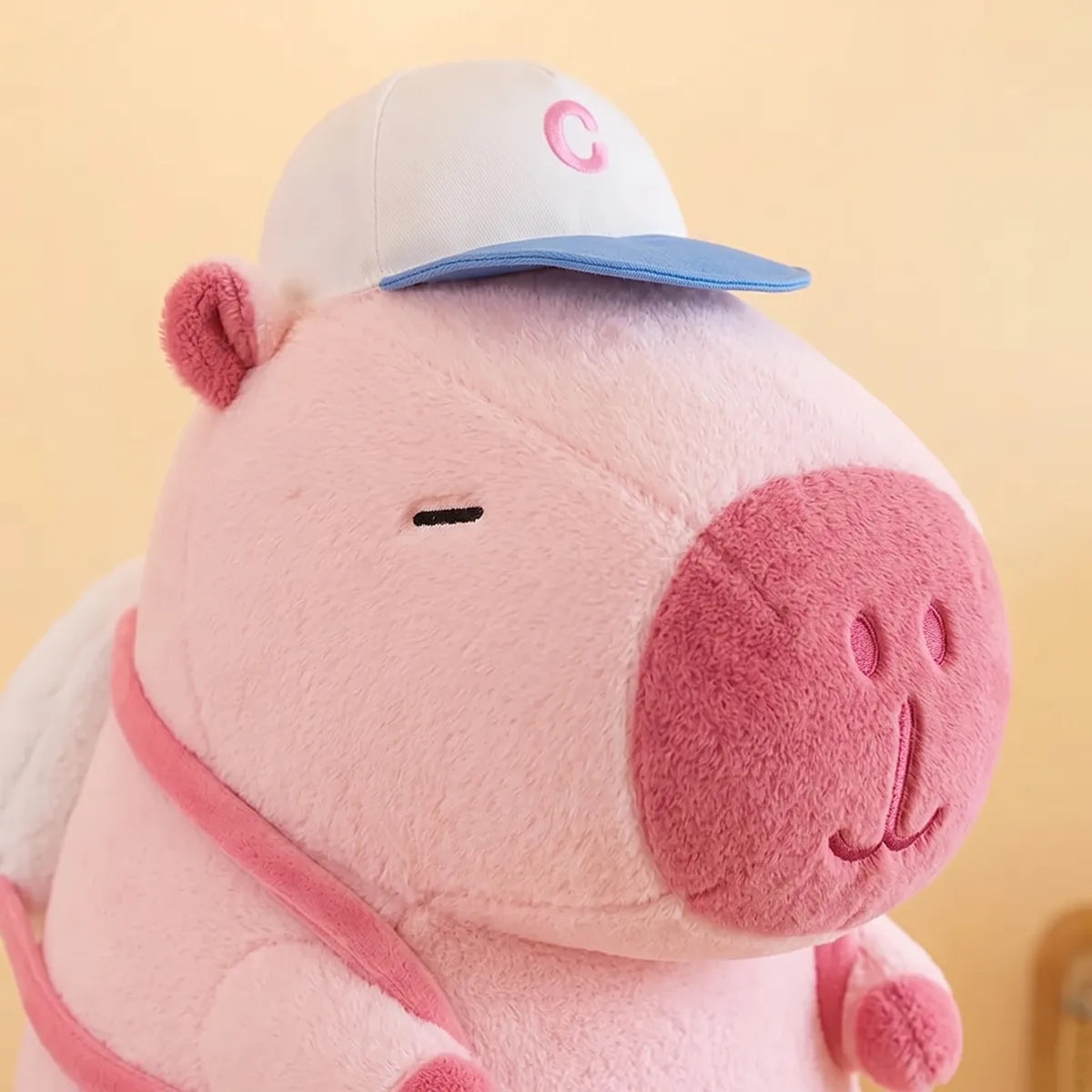 Close up of the rose muzzle and the white and blue cap on the pink capybara plush
