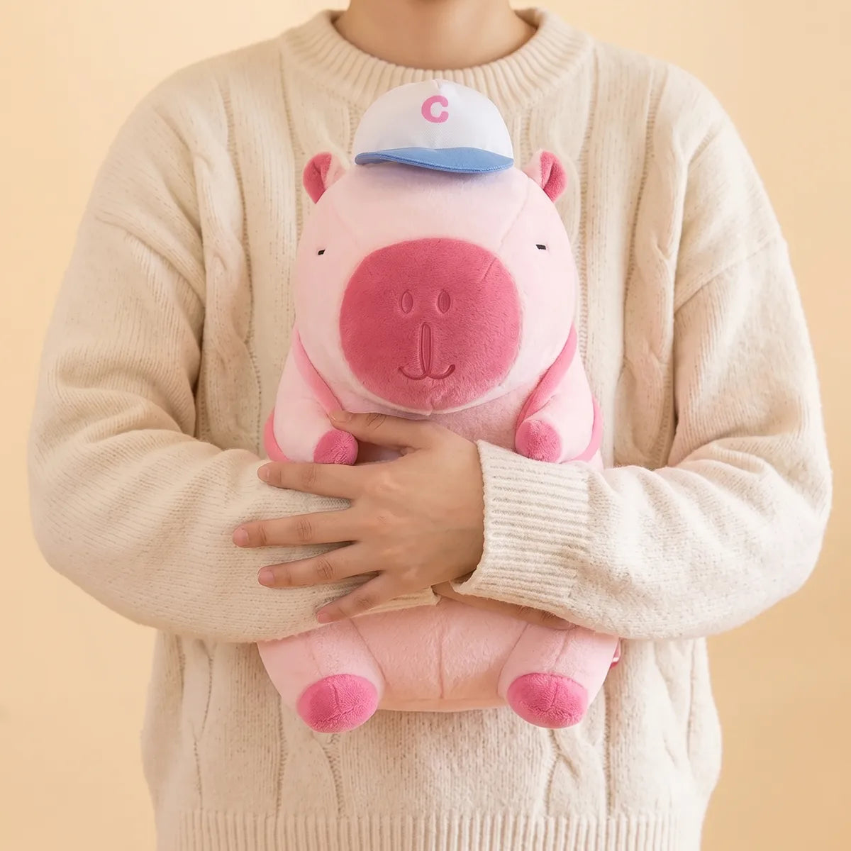 Person hugging the pink baseball backpack capybara plush against a sweater