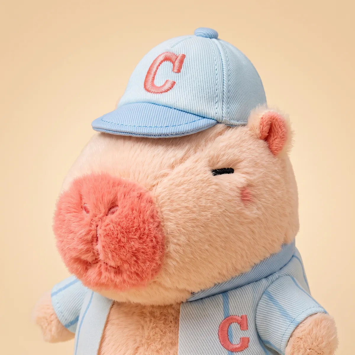 Close up of the pink baseball mini capybara plush cap with a coral C and fuzzy muzzle