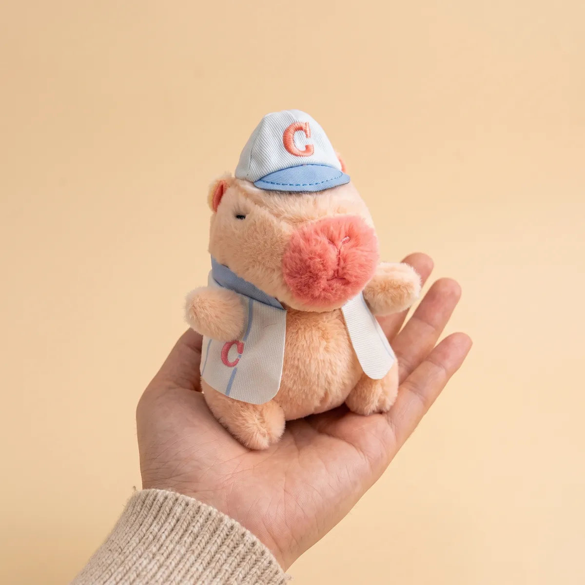 Pink baseball mini capybara plush resting in an open palm to show its 4 in size