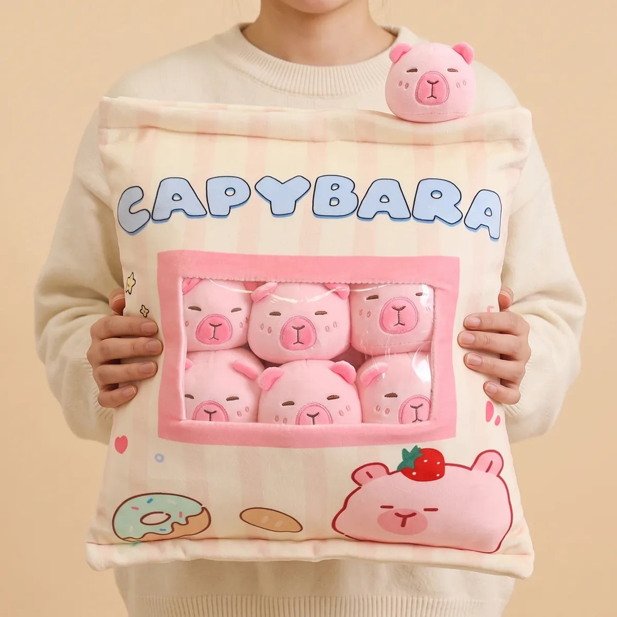 Person holding the pink mini capybara plush set against their chest with one mini balanced on their shoulder