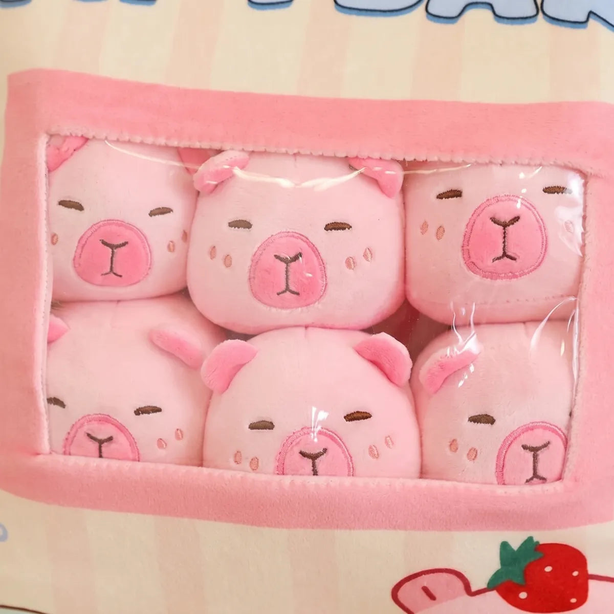 Close-up through the window at six pink mini capybara plush packed inside the snack bag pillow