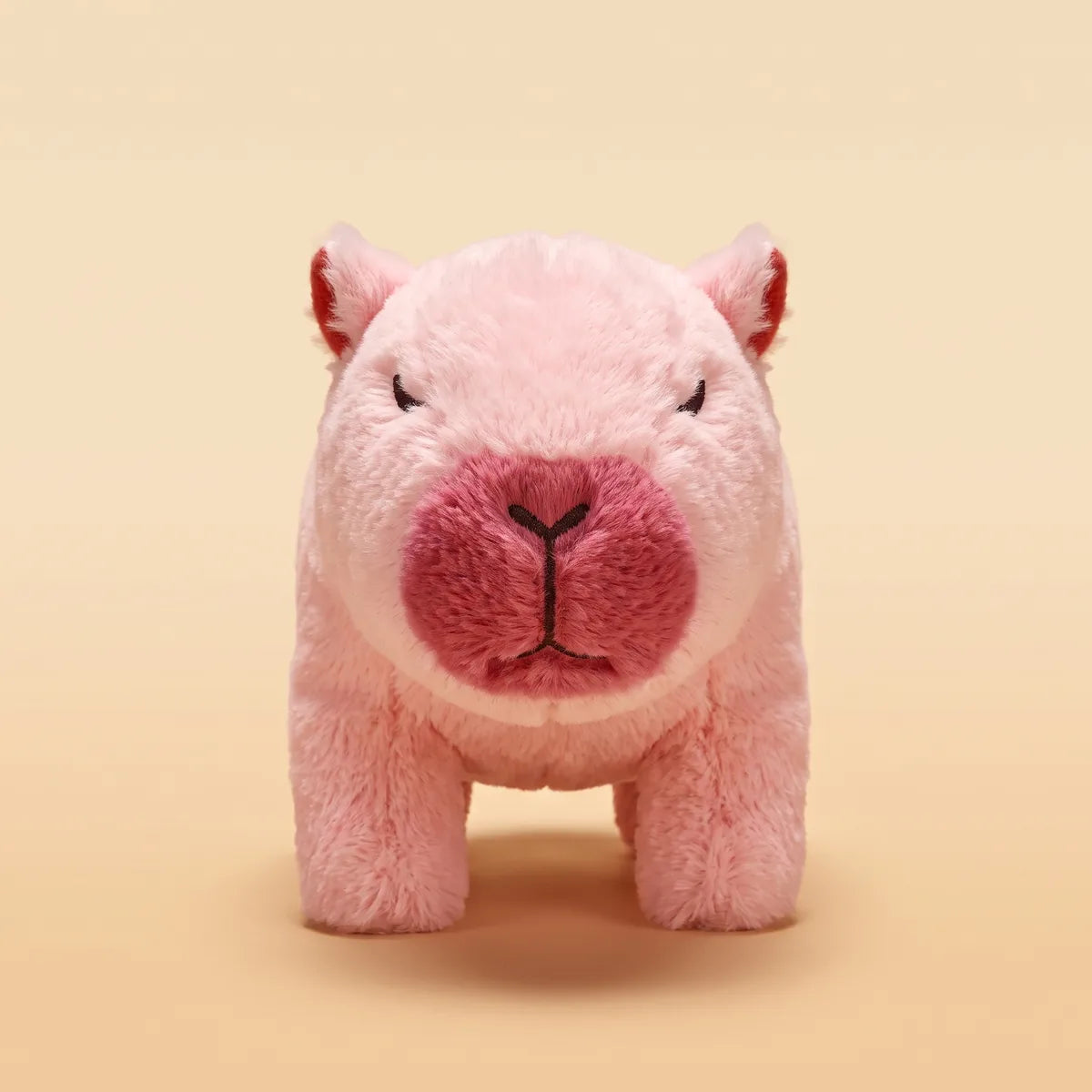 Front view of the pale pink walking capybara toy showing its raspberry snout and crimson inner ears