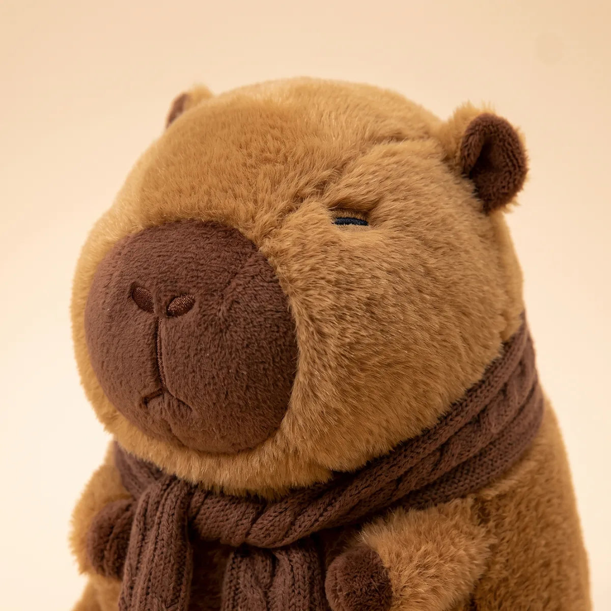 Close up of the scarf capybara plush face with a dark chocolate muzzle