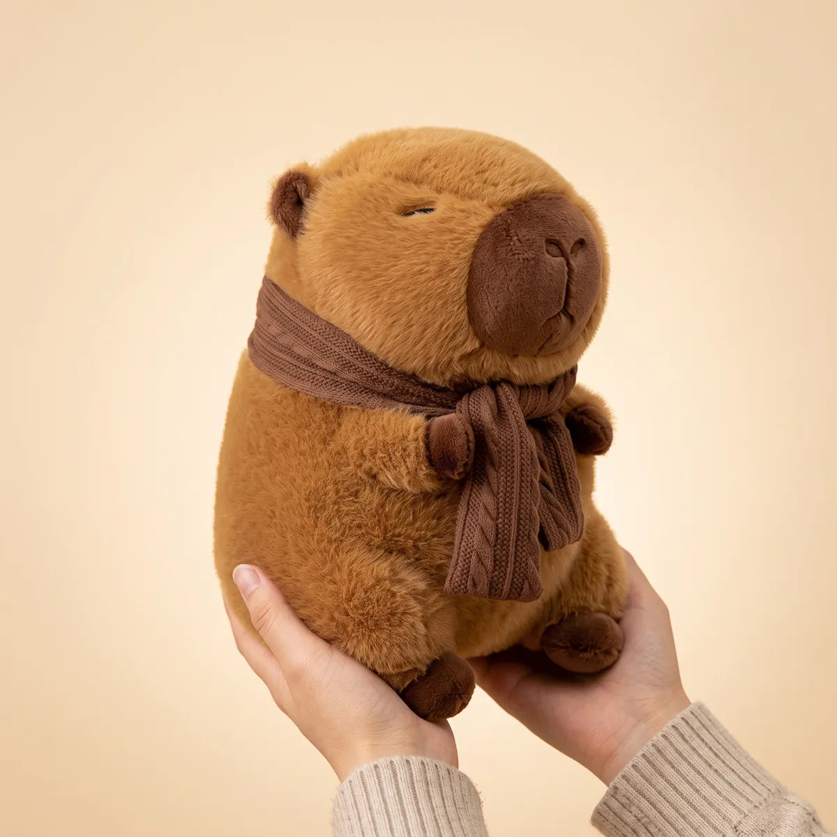 Scarf capybara plush held in two hands to show the 10 in and 12 in scale
