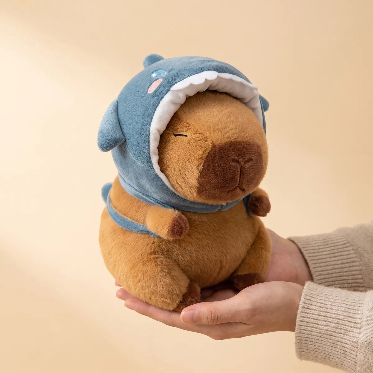 Hands holding the 9 in (22 cm) shark hat capybara plush to show its real size