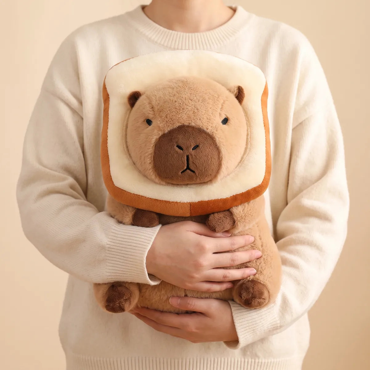 Person hugging the slice of bread capybara plush against a sweater