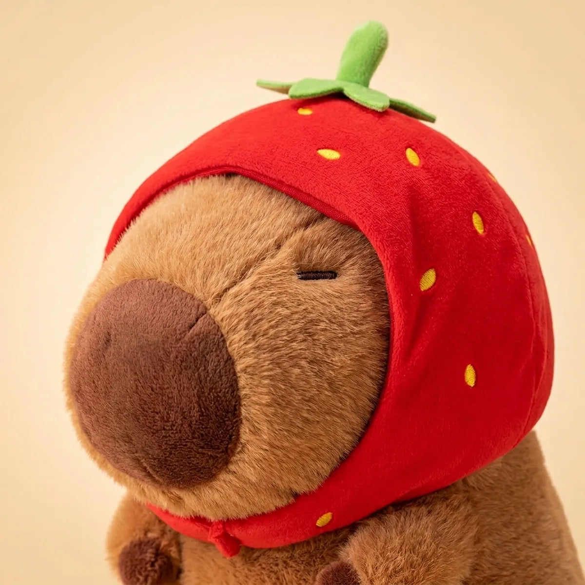 Close up of the strawberry capybara plush face with its embroidered eyes and nose under the berry hood