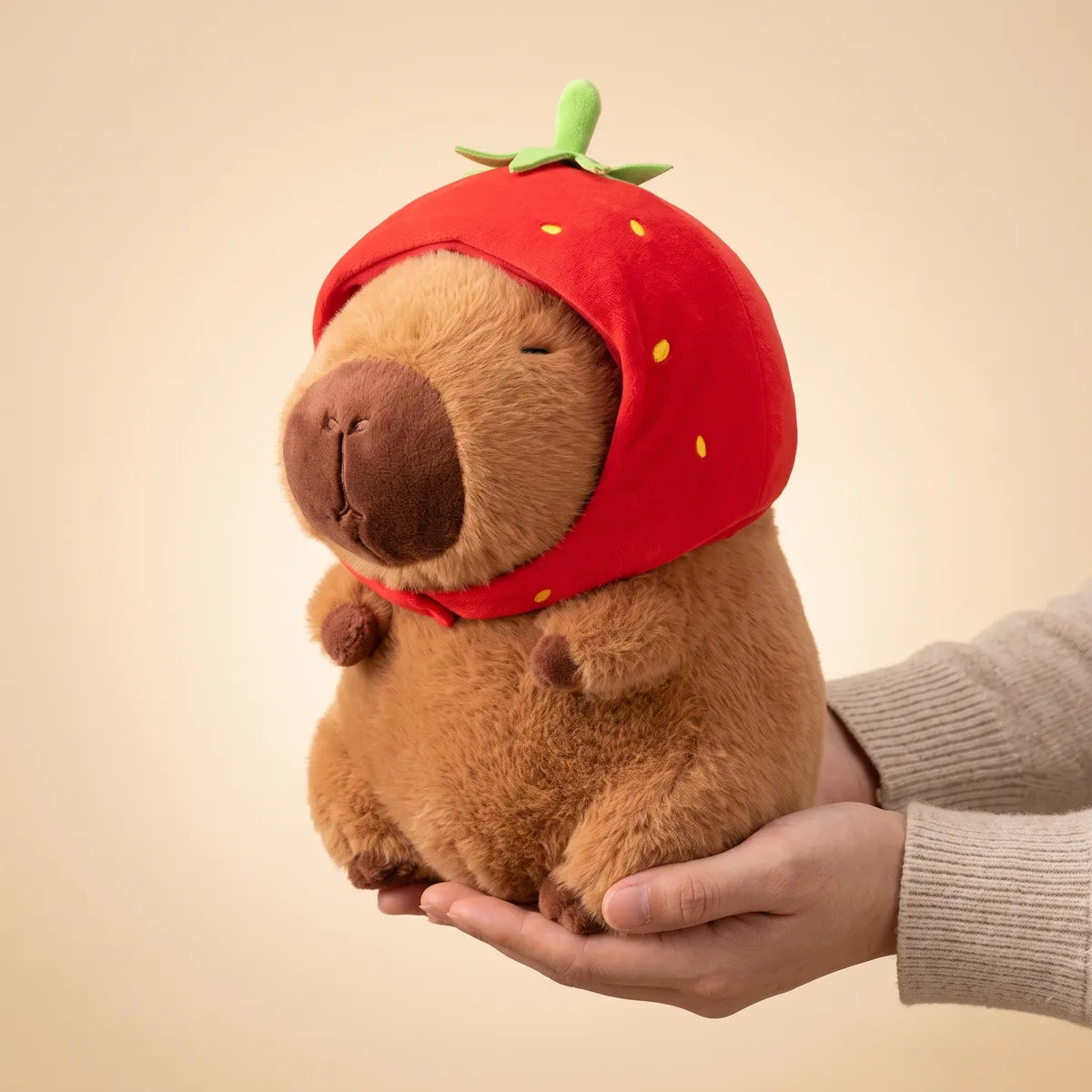 Hands holding the 9 in strawberry capybara plush to show its real size
