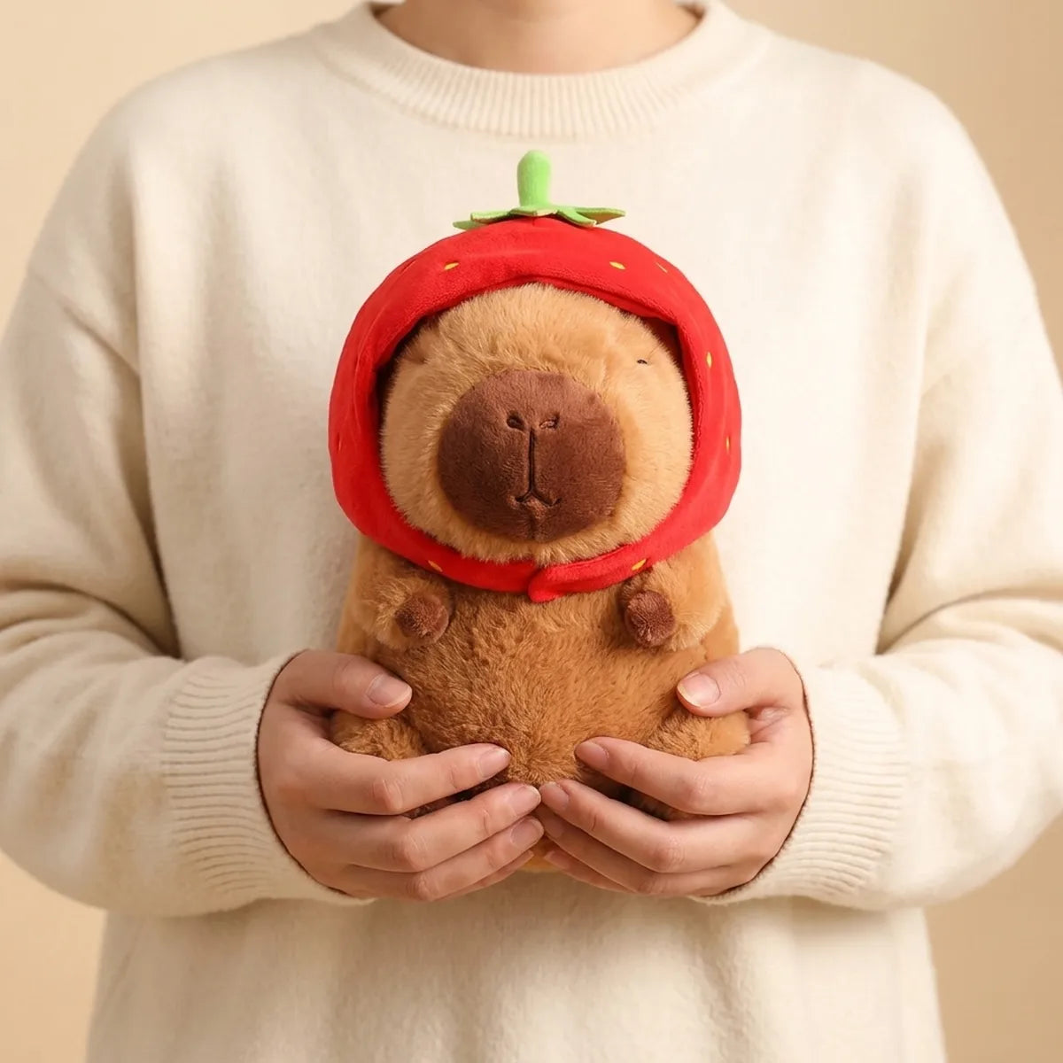 Person hugging the strawberry capybara plush against a cream knit sweater