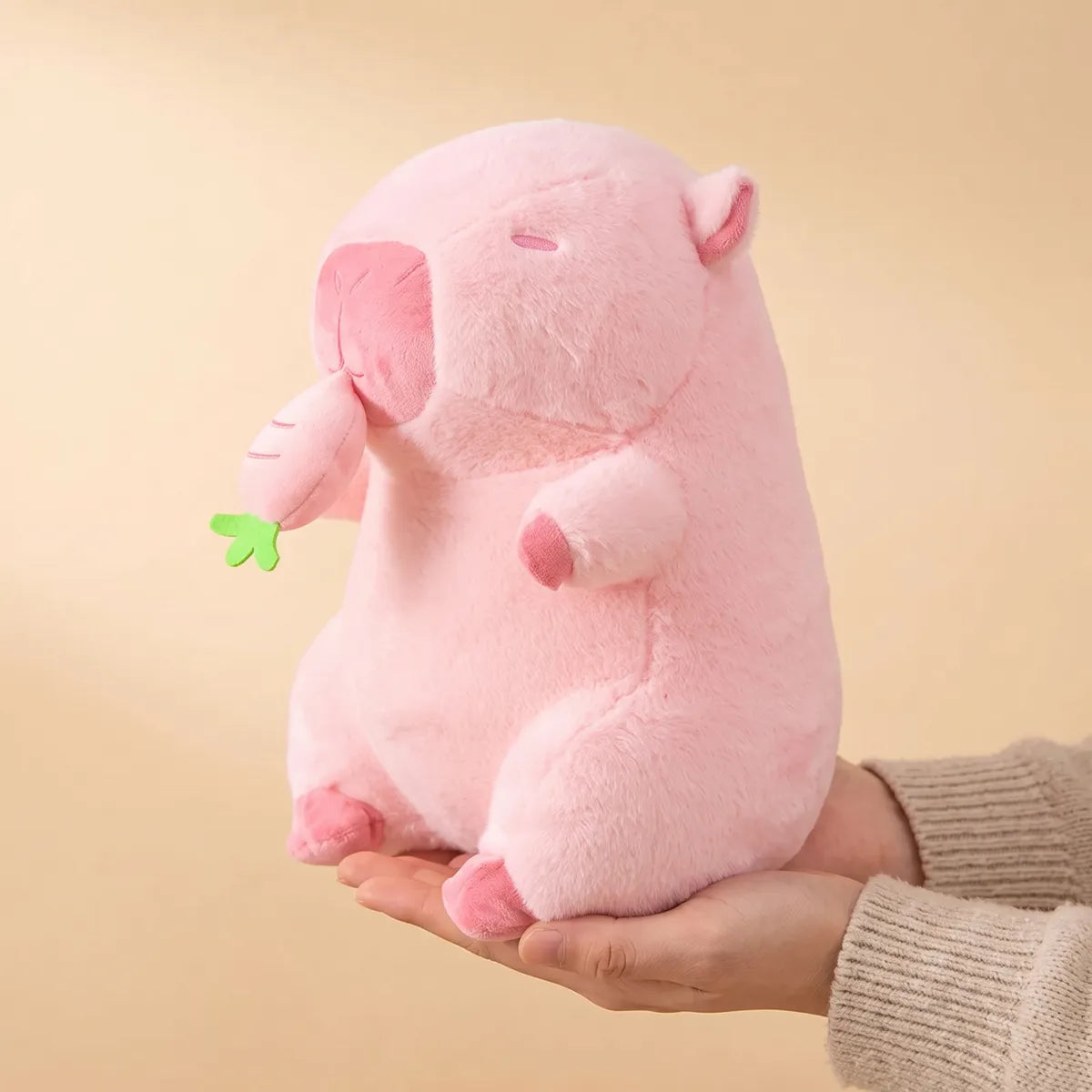 Pink capybara plush resting upright on an open palm to show its 12 in seated height