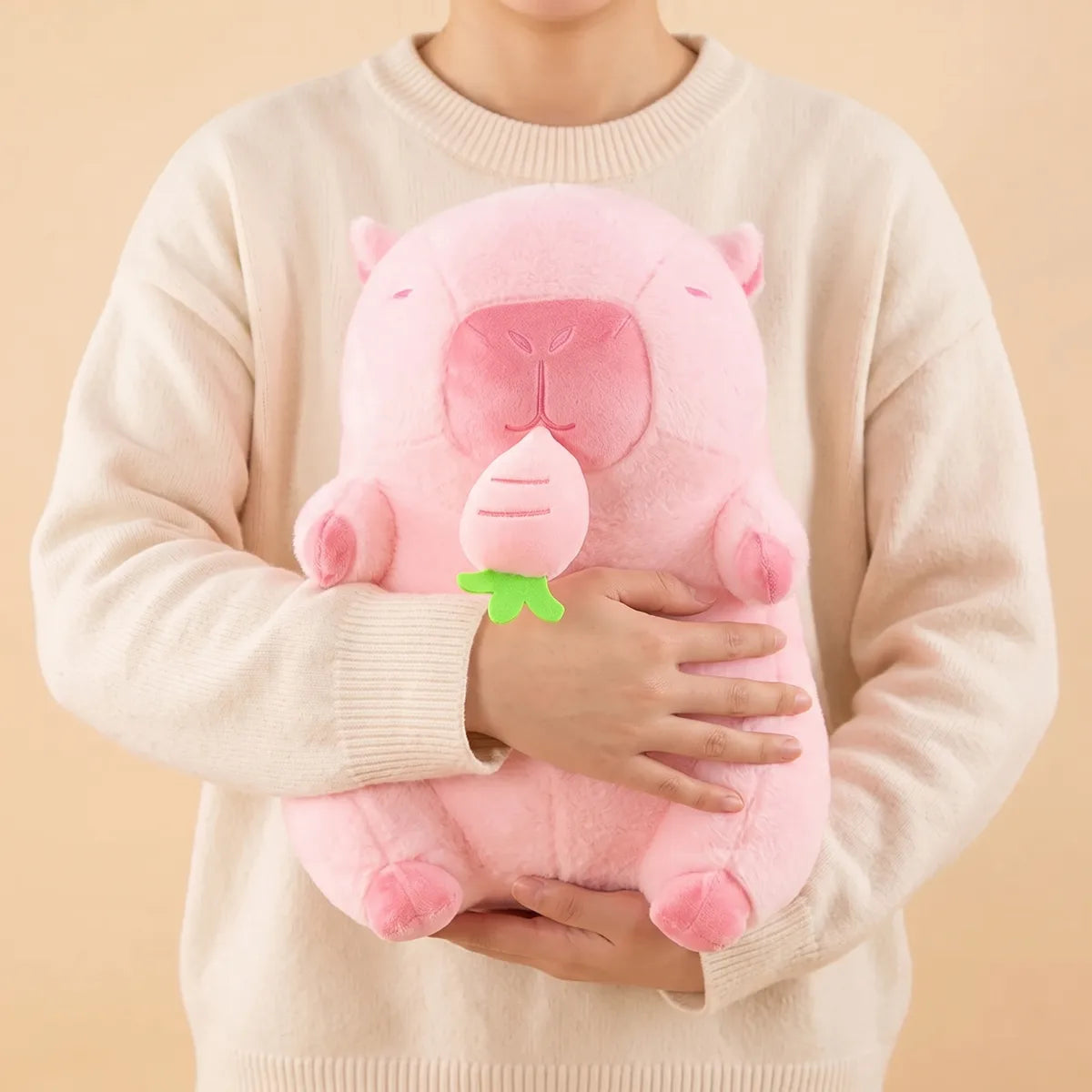 Person in a cream sweater holding the pink capybara plush against their chest with both arms