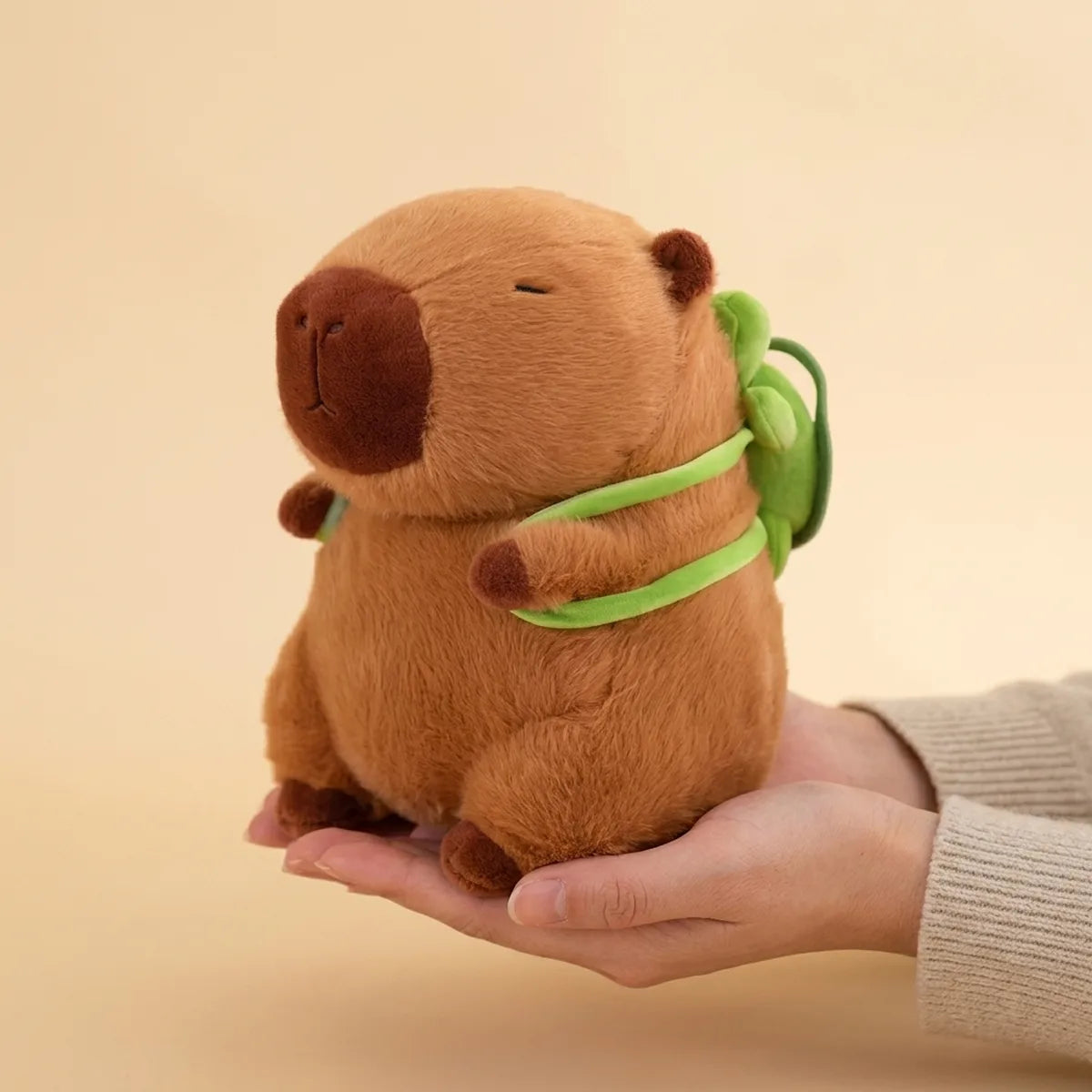 Hands cradling the turtle backpack capybara plush to show its real size