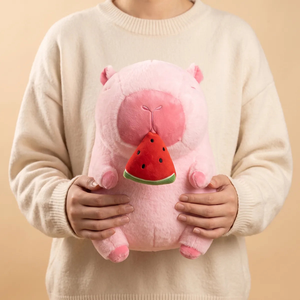 Watermelon capybara plush held in both hands against a cream knit sweater