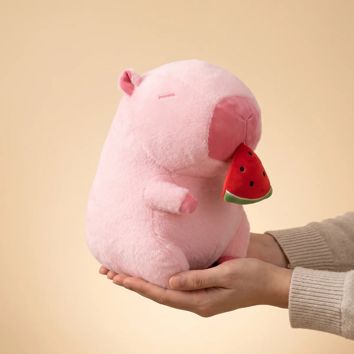Watermelon capybara plush resting on one open hand to show its 12 in height
