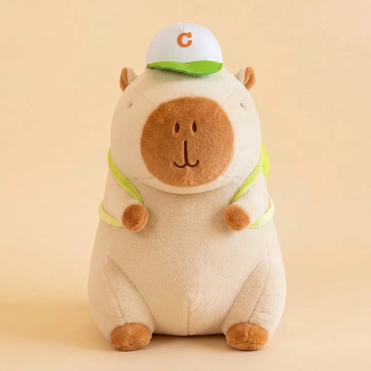 Cream white capybara plush with a green cap and lime backpack straps seen from the front